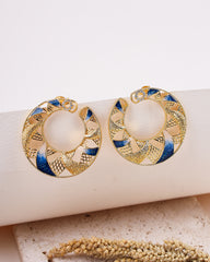 Gold and blue earrings on a white surface with a natural background