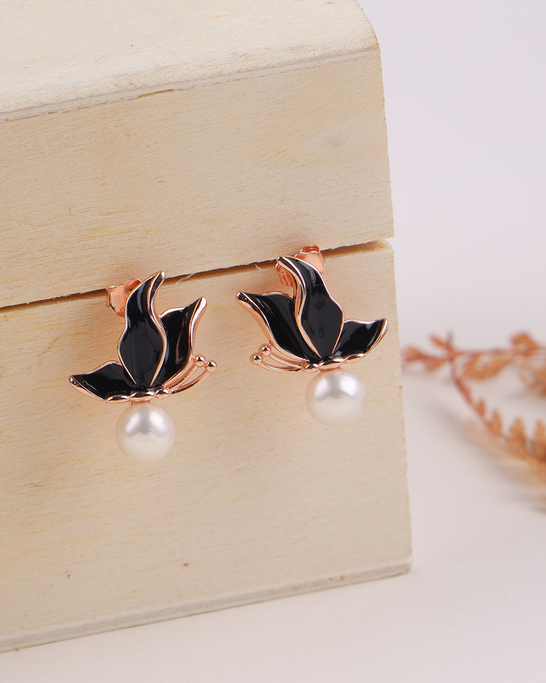 Rose gold and black leaf-shaped earrings on a wooden box.