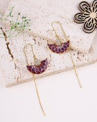 Purple and gold earrings on a textured stone surface with a decorative flower.