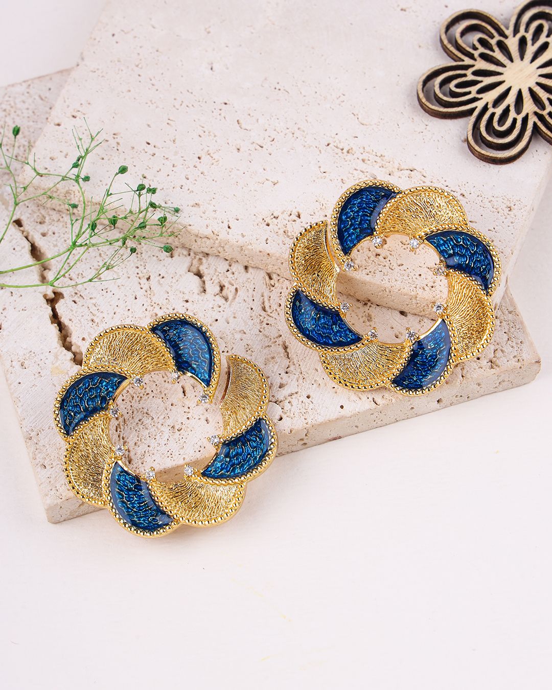 Pair of gold and blue earrings on a textured surface with a decorative background