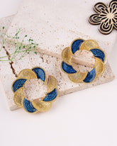 Pair of gold and blue earrings on a textured surface with a decorative background