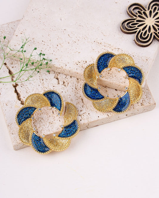 Pair of gold and blue earrings on a textured surface with a decorative background