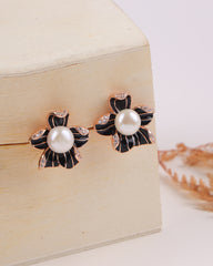 Pair of pearl earrings with black and gold floral designs on a wooden box.