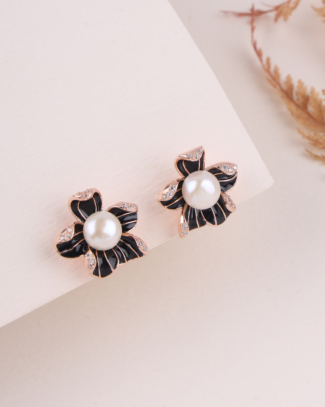 Pair of pearl earrings with black floral designs on a light background