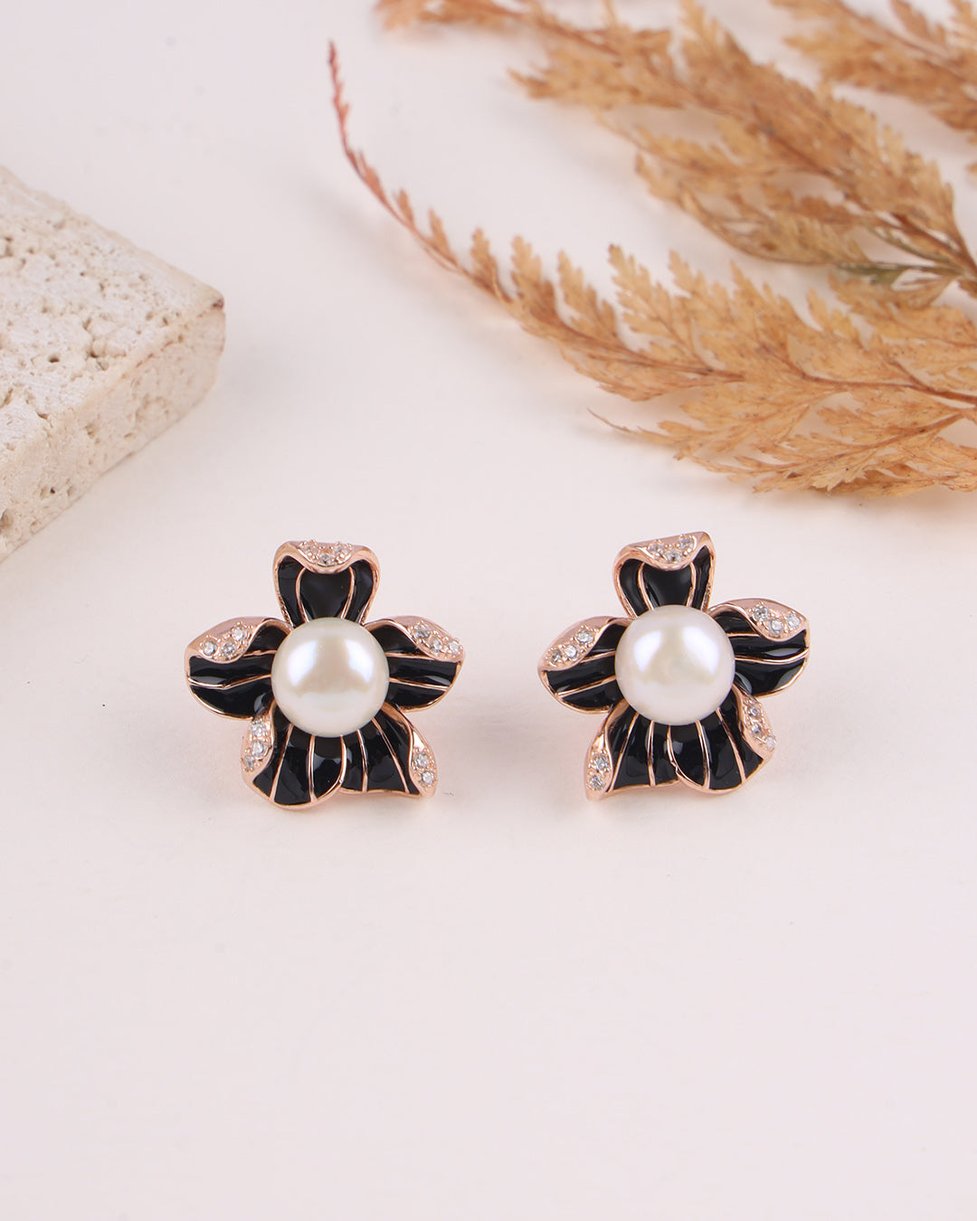 Pair of black and gold flower-shaped earrings with pearls on a light background.