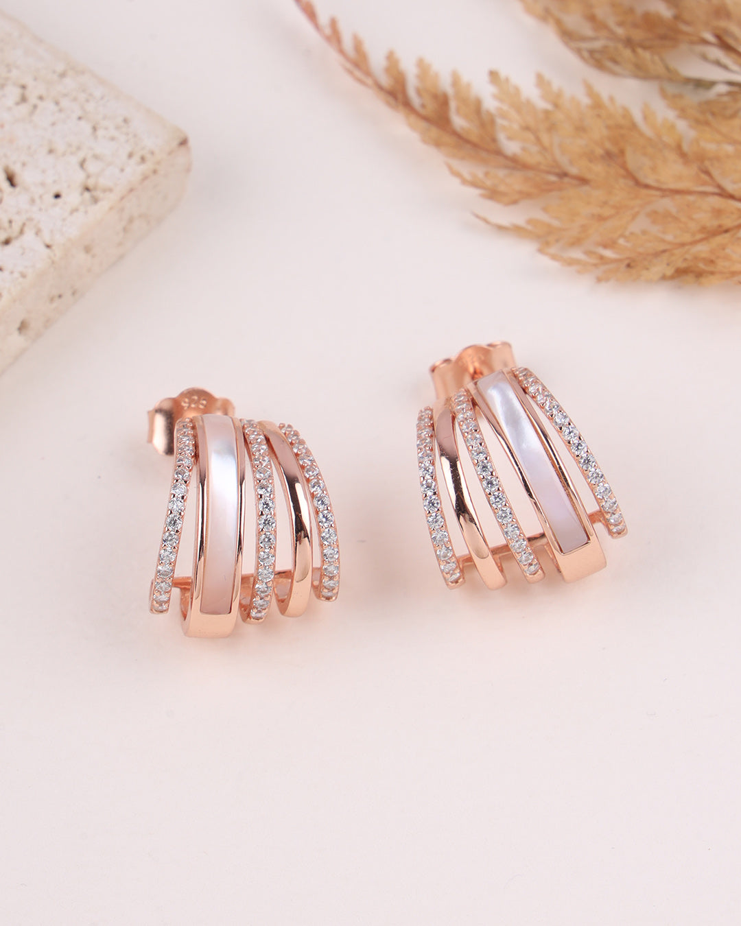 Rose gold and silver hoop earrings on a light background with dried plants.