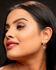 Close-up of a woman wearing a diamond-shaped earring against a dark background