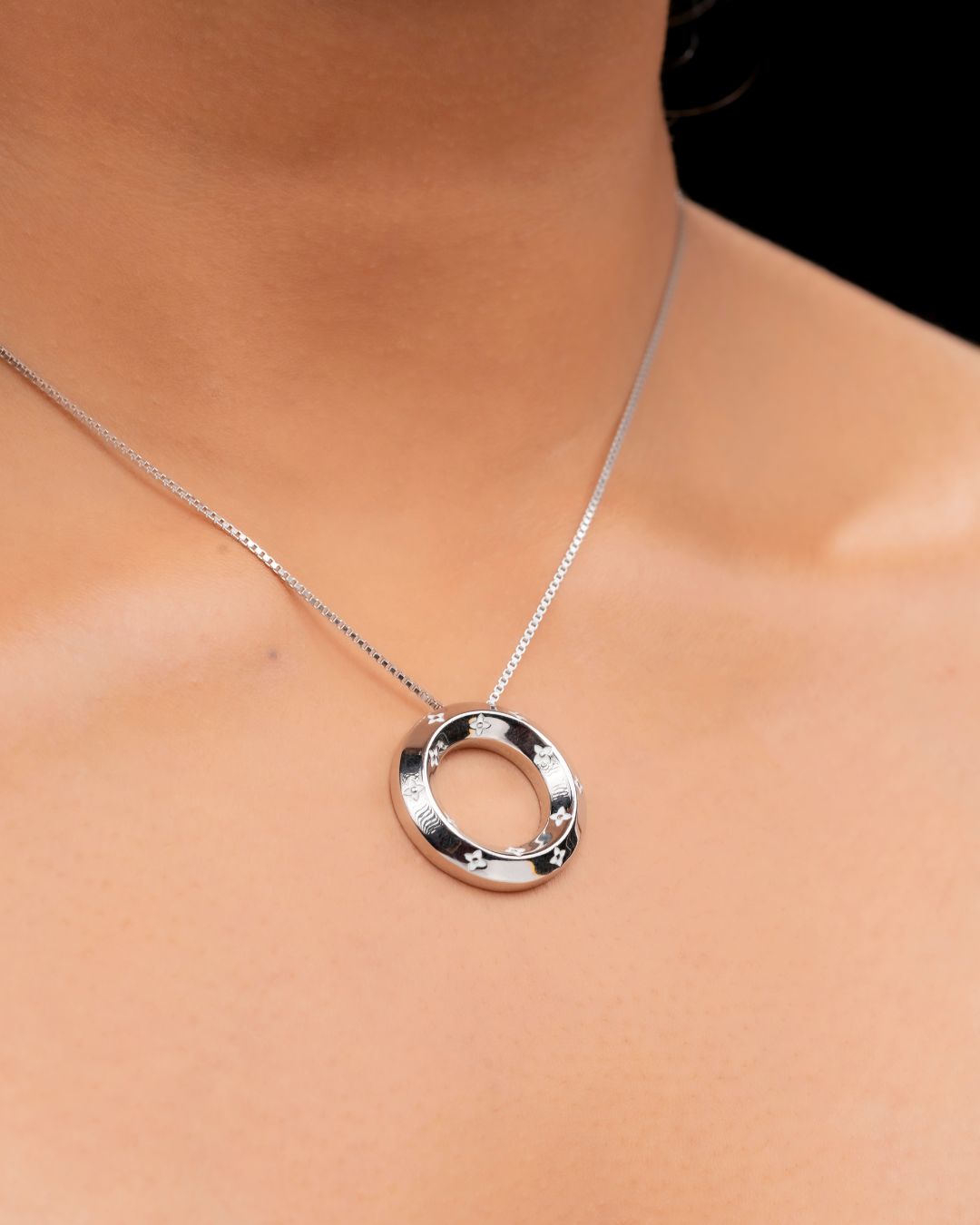 Silver necklace with a circular pendant on a person's neck against a neutral background