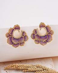 Pair of purple and gold earrings on a white surface with a natural background