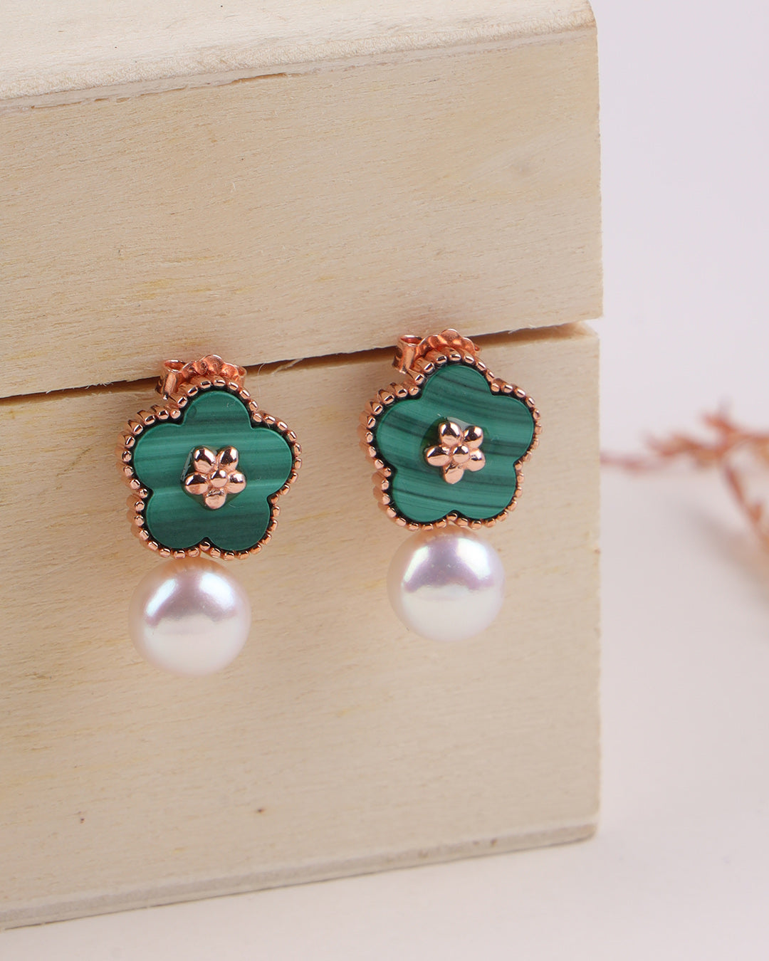Pair of earrings with green floral designs and pearl-like bottoms on a wooden surface.