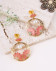 Pair of floral earrings with pink flowers and gold accents on a textured surface.