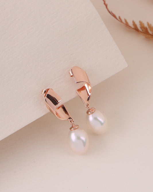 Rose gold earrings with pearl drops on a light background