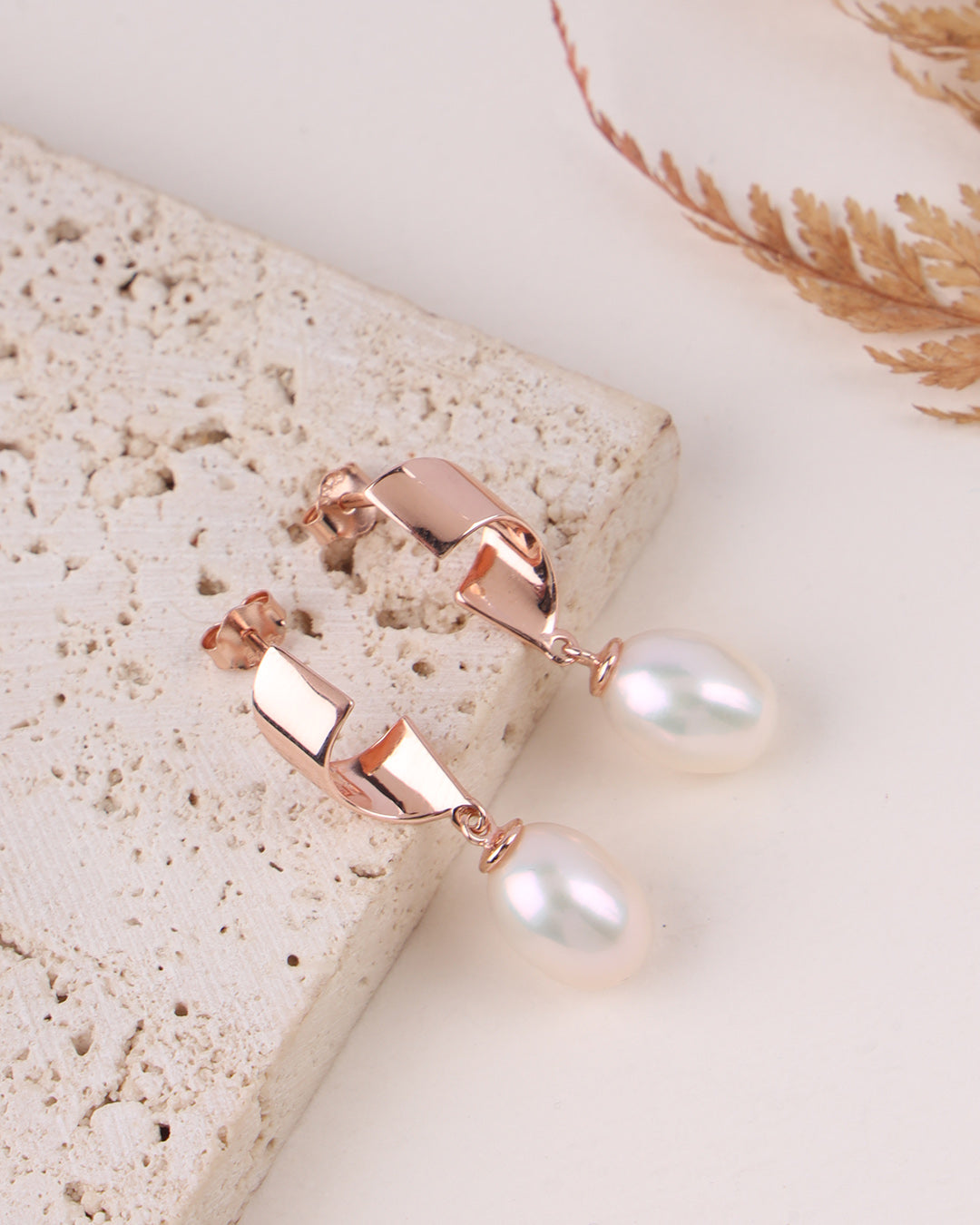 Rose gold earrings with pearls on a light stone surface