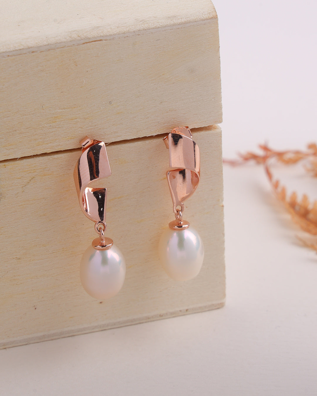 Rose gold earrings with pearl drops on a wooden box