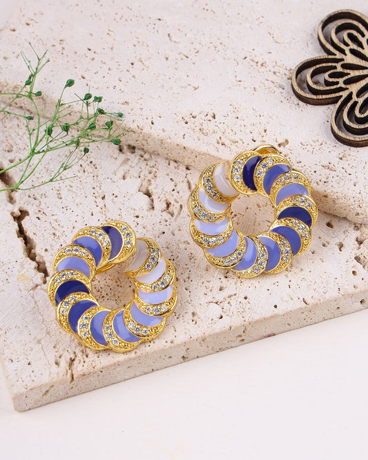 Pair of hoop earrings with blue and gold design on a textured surface.