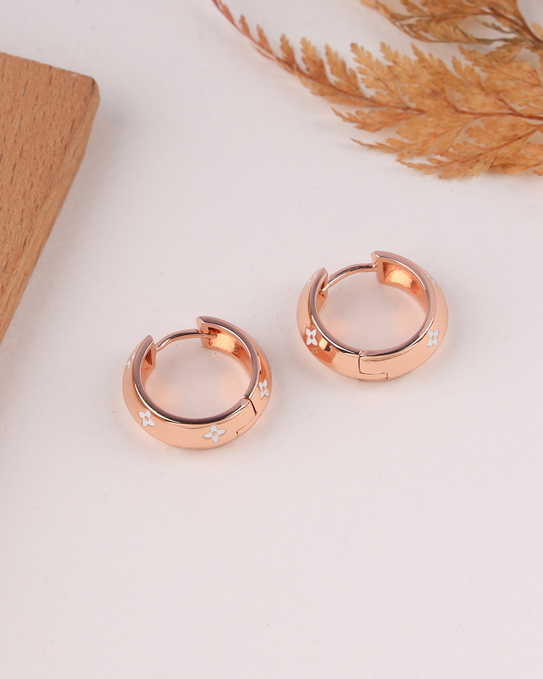 Rose gold hoop earrings on a light surface with dried plants in the background