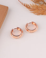 Rose gold hoop earrings on a light surface with dried plants in the background