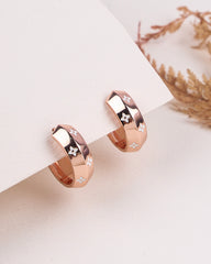 Two rose gold bali with star designs on a white surface.
