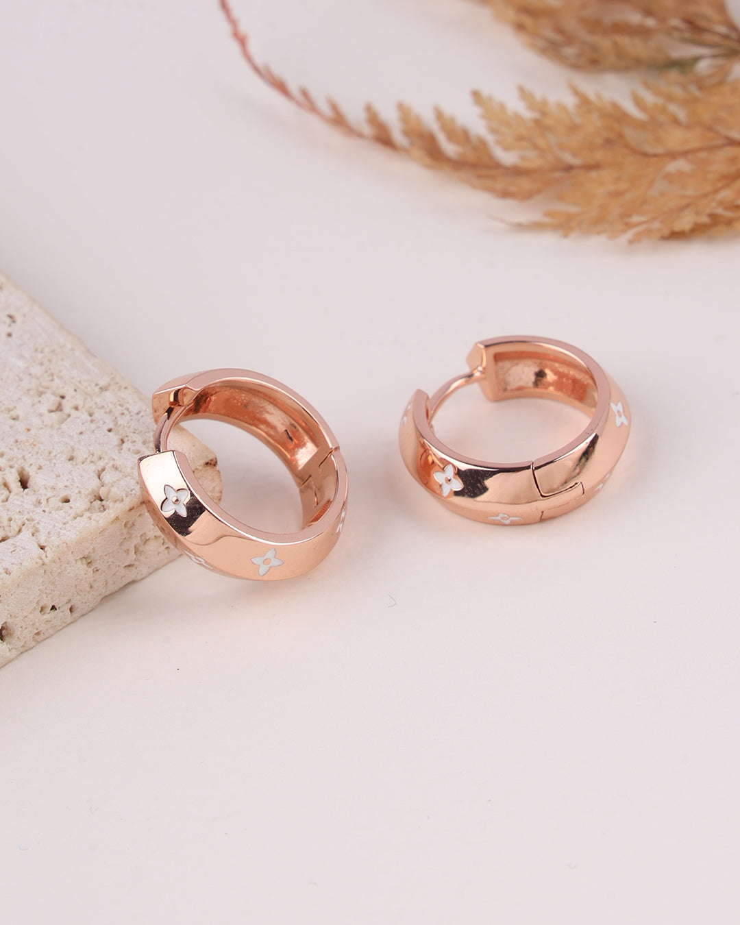 Rose gold hoop earrings on a light surface with decorative elements.