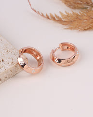 Rose gold hoop earrings on a light surface with decorative elements.