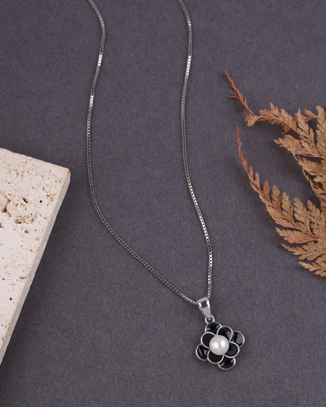 Silver necklace with a flower pendant on a dark surface