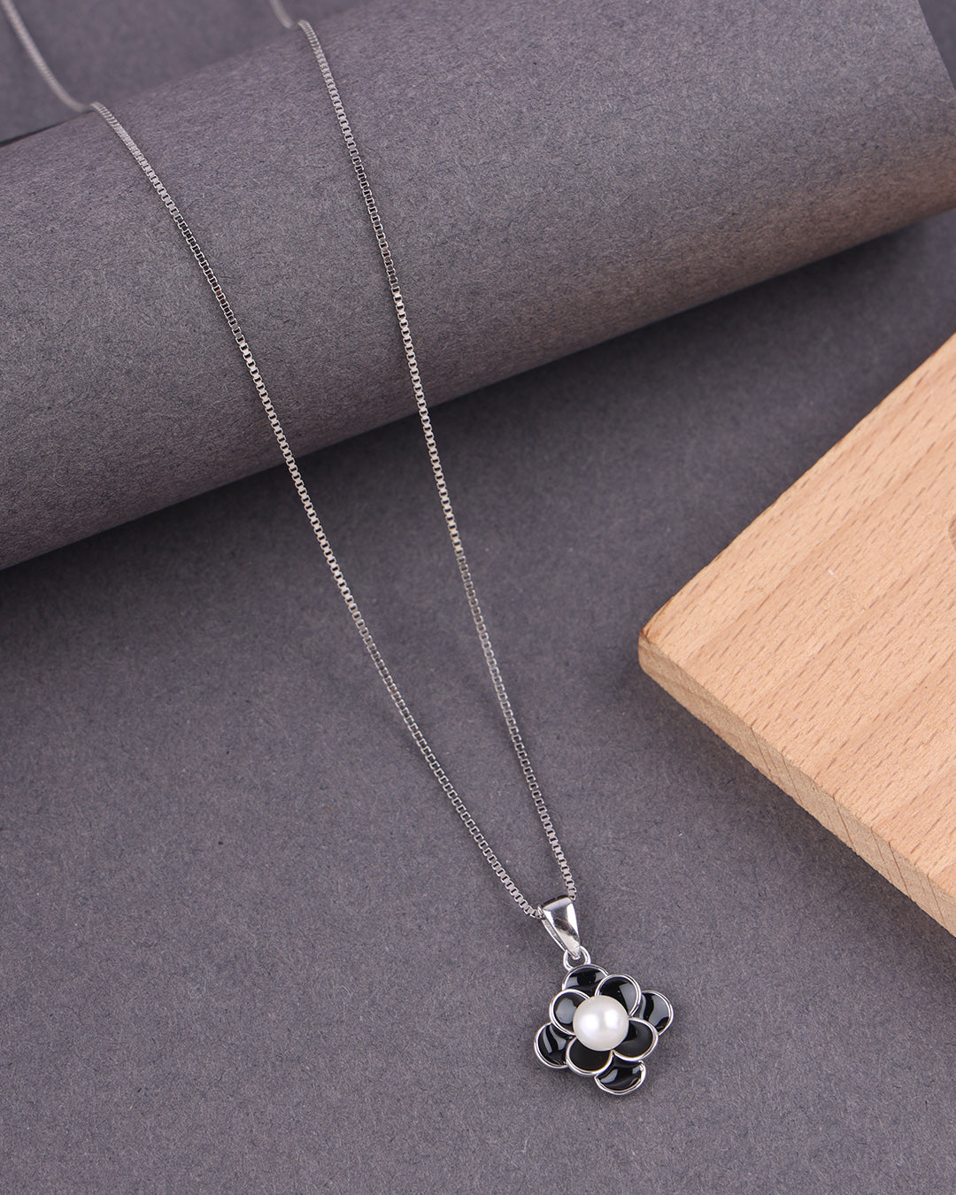 Silver necklace with a pendant featuring a pearl on a gray surface.