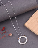Silver necklace with a circular pendant on a gray surface with dried flowers and a wooden block.