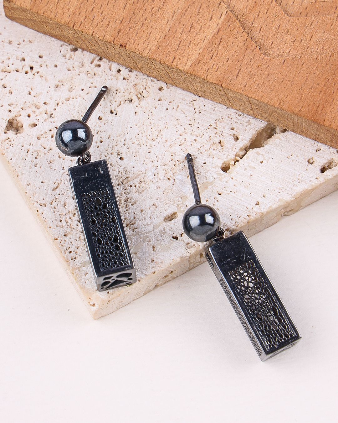 Black textured earrings with spherical beads on a stone surface