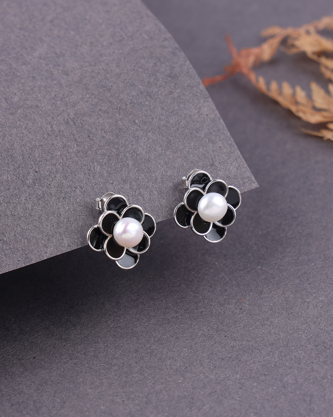 Flower-shaped earrings with pearl centers on a gray surface