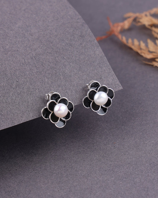 Flower-shaped earrings with pearl centers on a gray surface