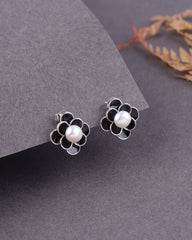 Flower-shaped earrings with pearl centers on a gray surface