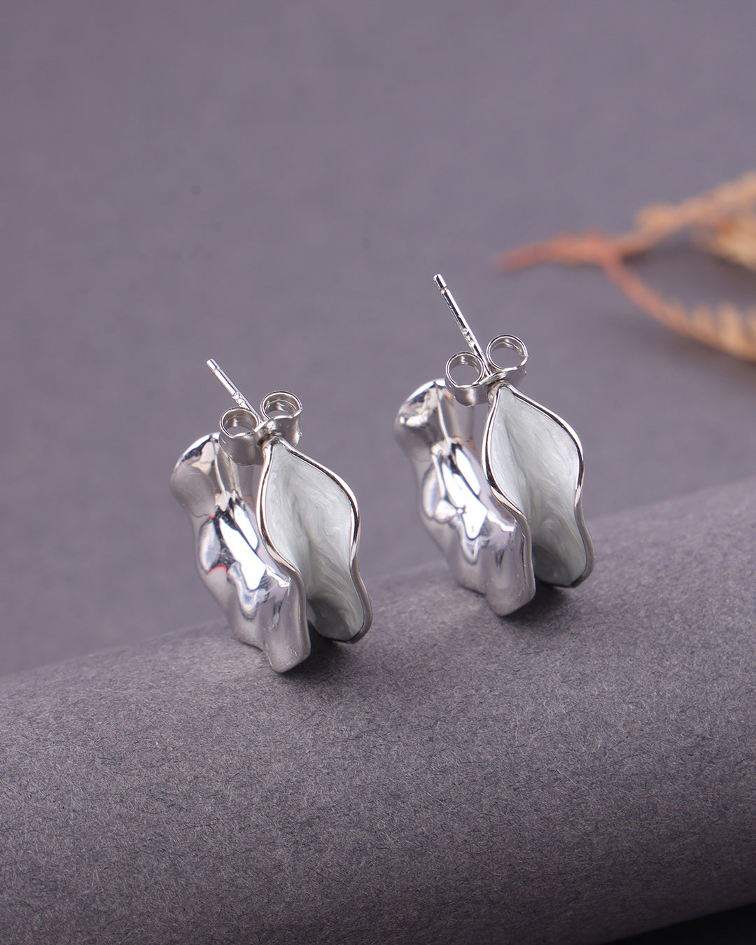 Silver leaf-shaped earrings on a gray surface