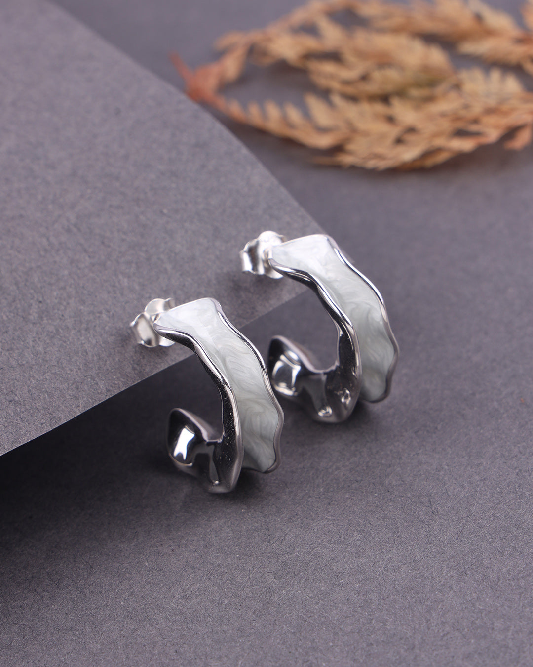 Pair of silver hoop earrings on a gray surface with dried leaves in the background