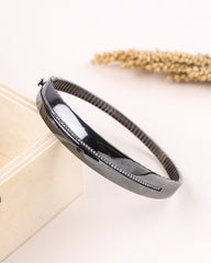 Black silver bracelet on a white surface with a beige book and dried plants in the background
