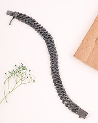 Gray braided bracelet on a white background with a wooden block and plant.