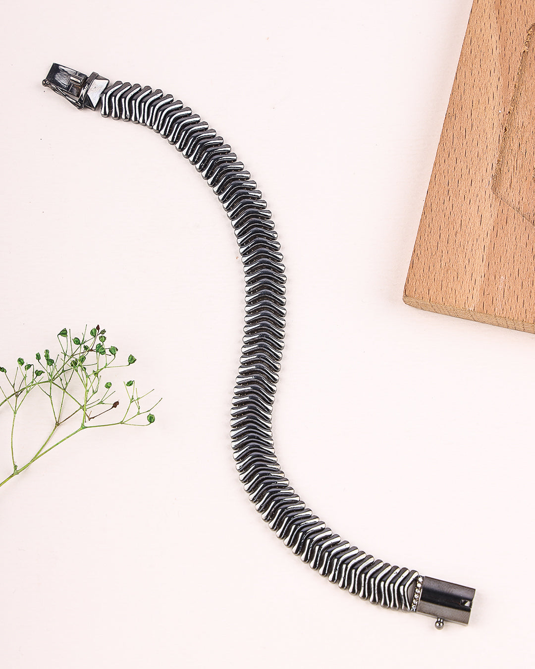 Black bracelet on a light surface with a wooden block and plant in the background