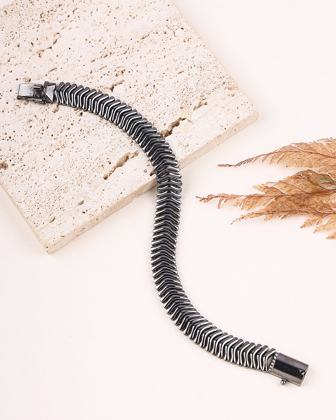 Black and silver striped bracelet on a textured surface with dried leaves.