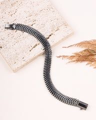 Black and silver striped bracelet on a textured surface with dried leaves.