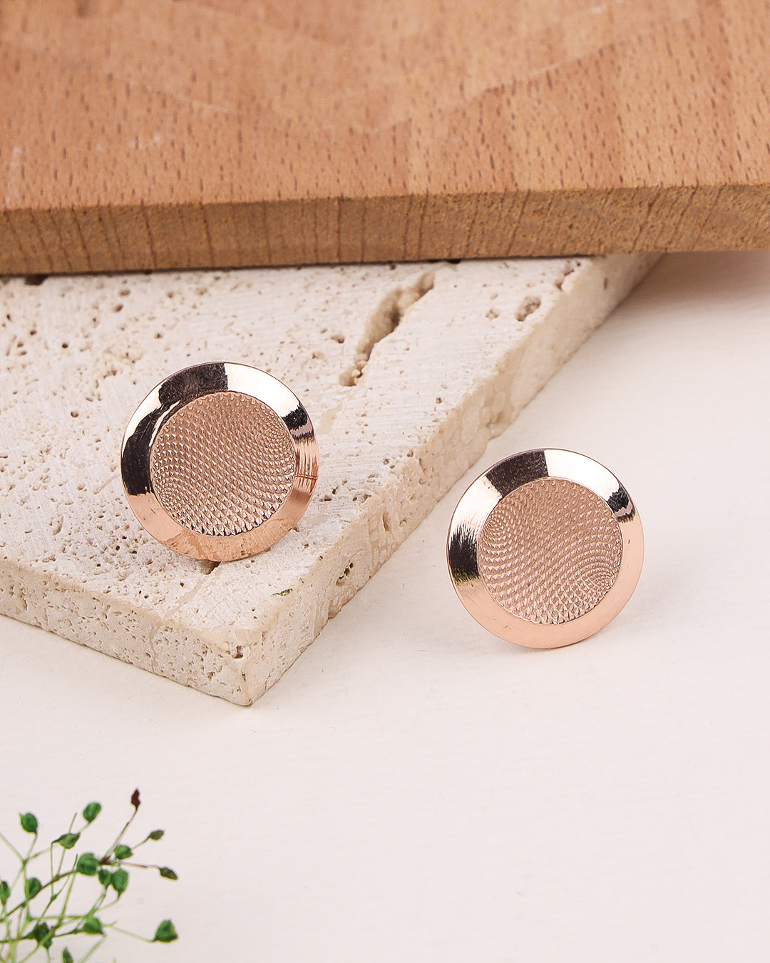 Rose gold earrings on a textured stone surface with a wooden box in the background.
