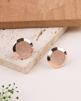 Rose gold earrings on a textured stone surface with a wooden box in the background.