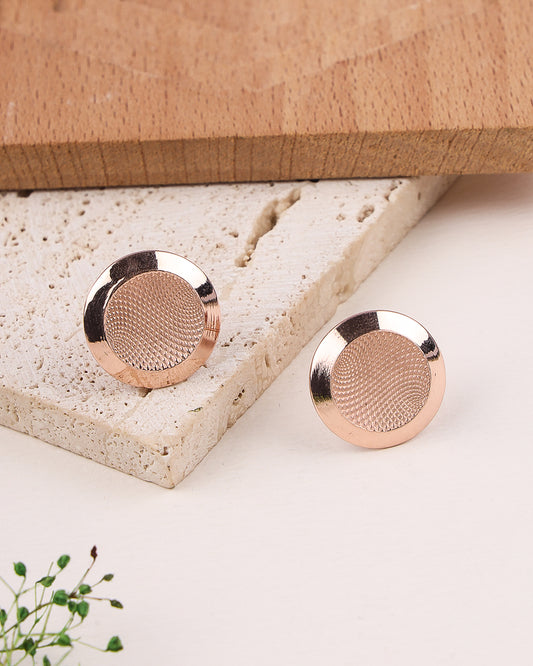 Rose gold earrings on a textured stone surface with a wooden box in the background.