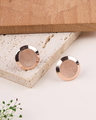 Rose gold earrings on a textured stone surface with a wooden box in the background.