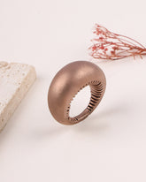 Rose gold silver ring on a light background with a piece of stone and dried plant.
