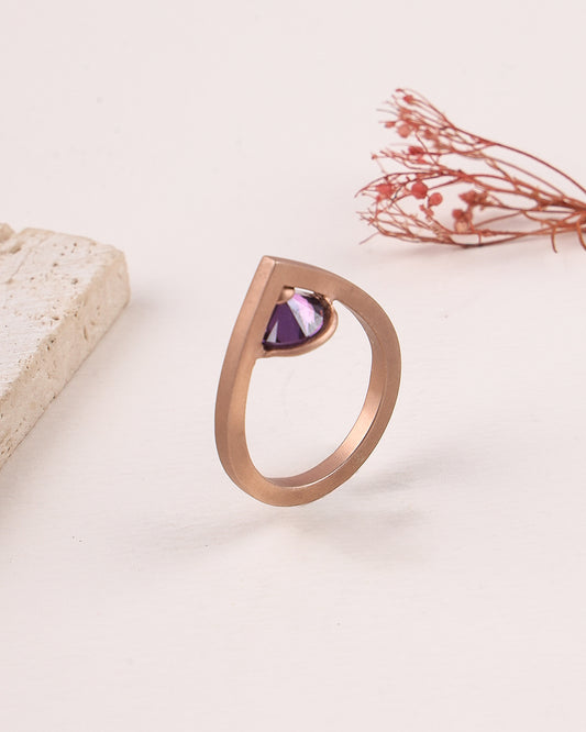 Rose gold ring with a purple gemstone on a light background