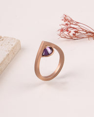 Rose gold ring with a purple gemstone on a light background