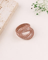 Rose gold filigree ring on a light surface with a stone and plant in the background