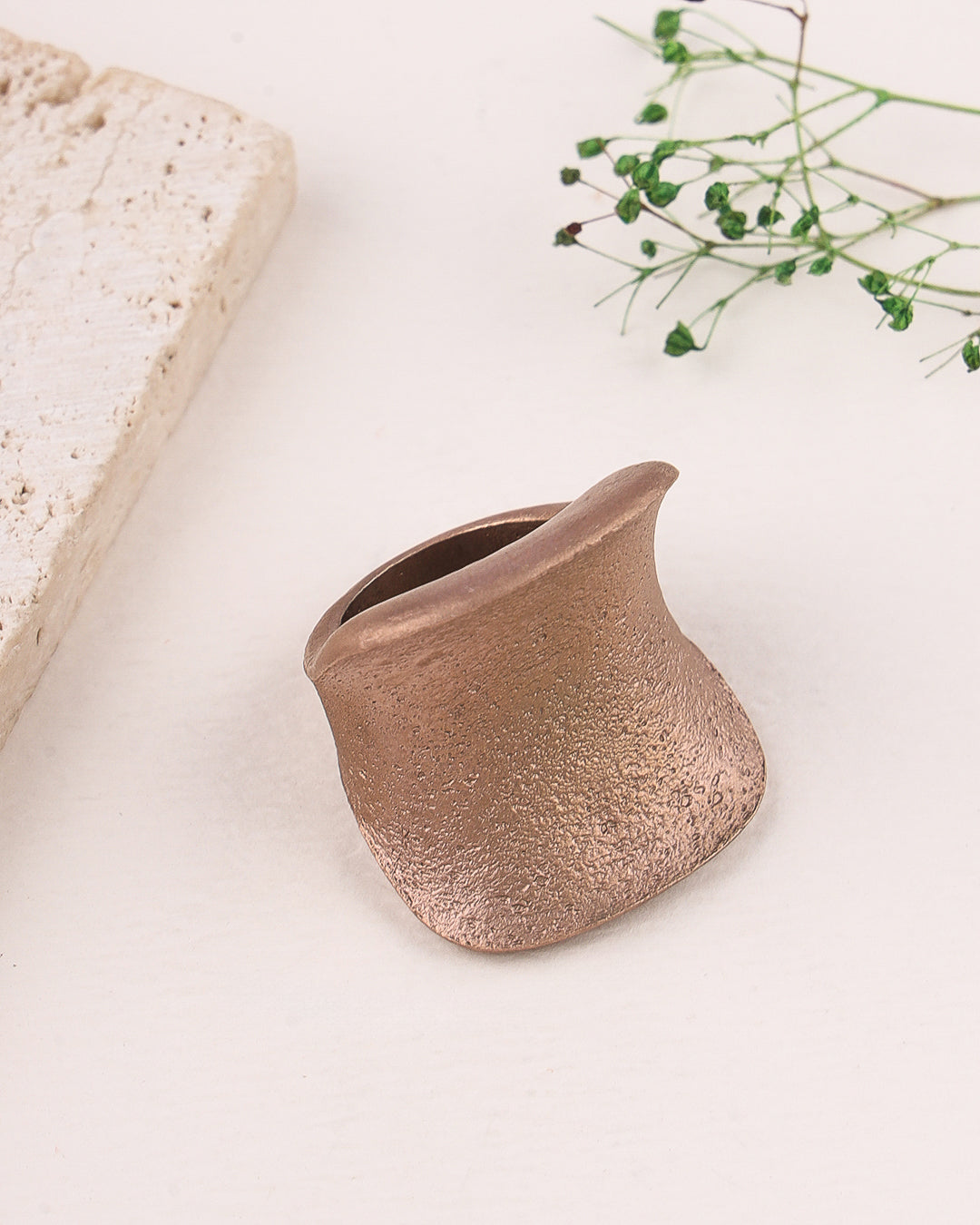 Rose gold ring on a light background with a piece of stone and greenery.