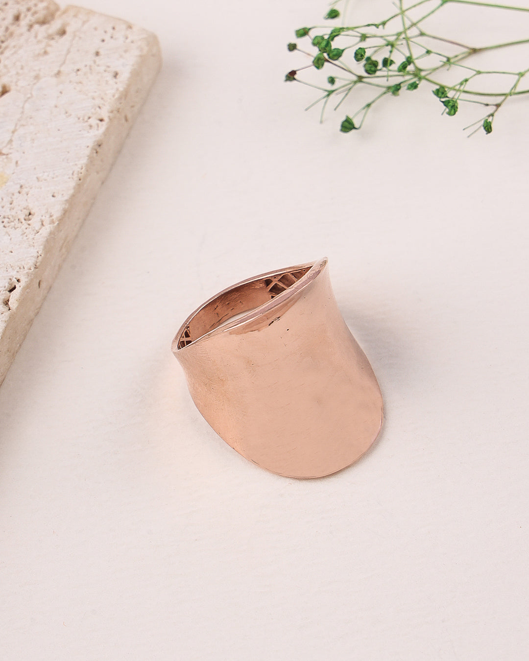 Rose gold ring on a light surface with a stone and greenery in the background