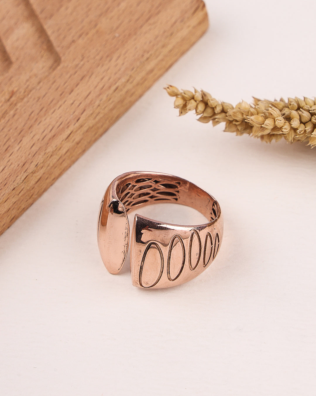 Rose gold ring with engraved text on a light surface with wooden and dried plant elements.