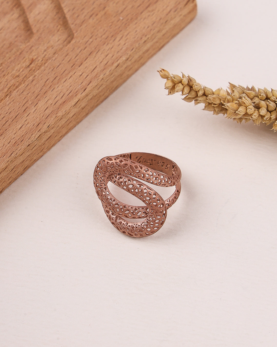 Rose gold filigree ring on a light surface with wooden block and dried plant